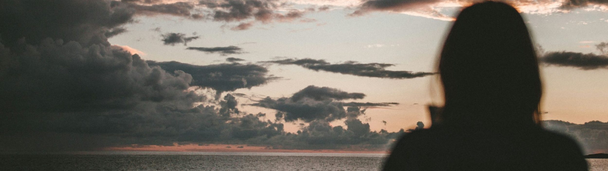 Donna di spalle che osserva l’orizzonte tra mare e cielo al tramonto